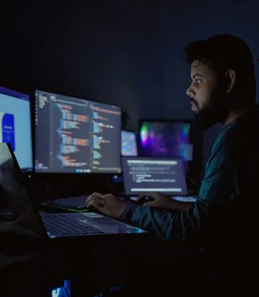 Security engineer analyzing code across multiple monitors at night