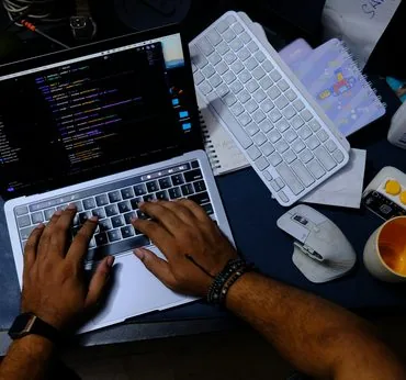 Close-up of hands typing on a laptop keyboard with code on screen