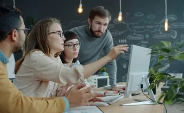 Team of colleagues collaborating around a computer in the office